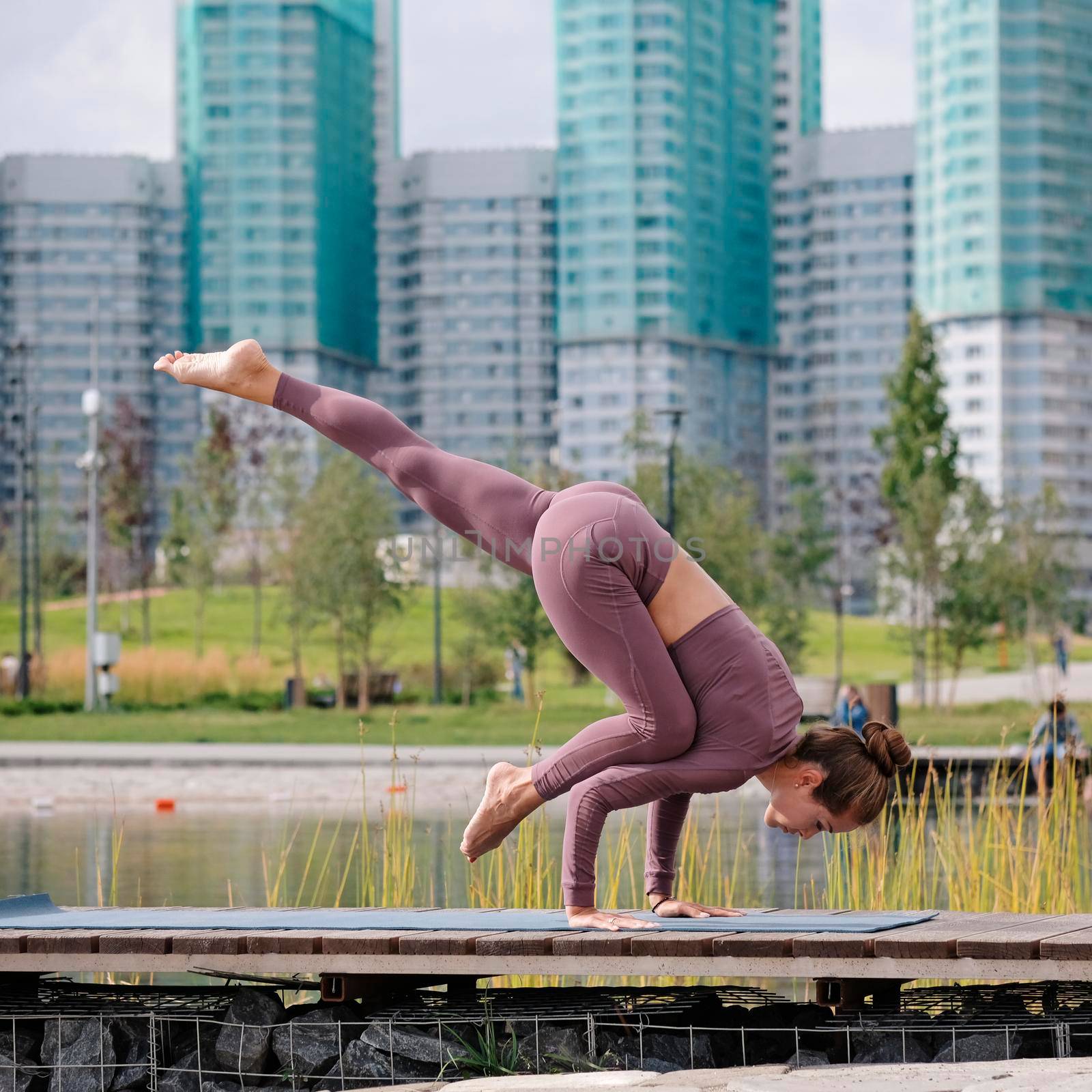 Young woman doing yoga exercises with city on background. eka pada kaundiniasana, balance pose