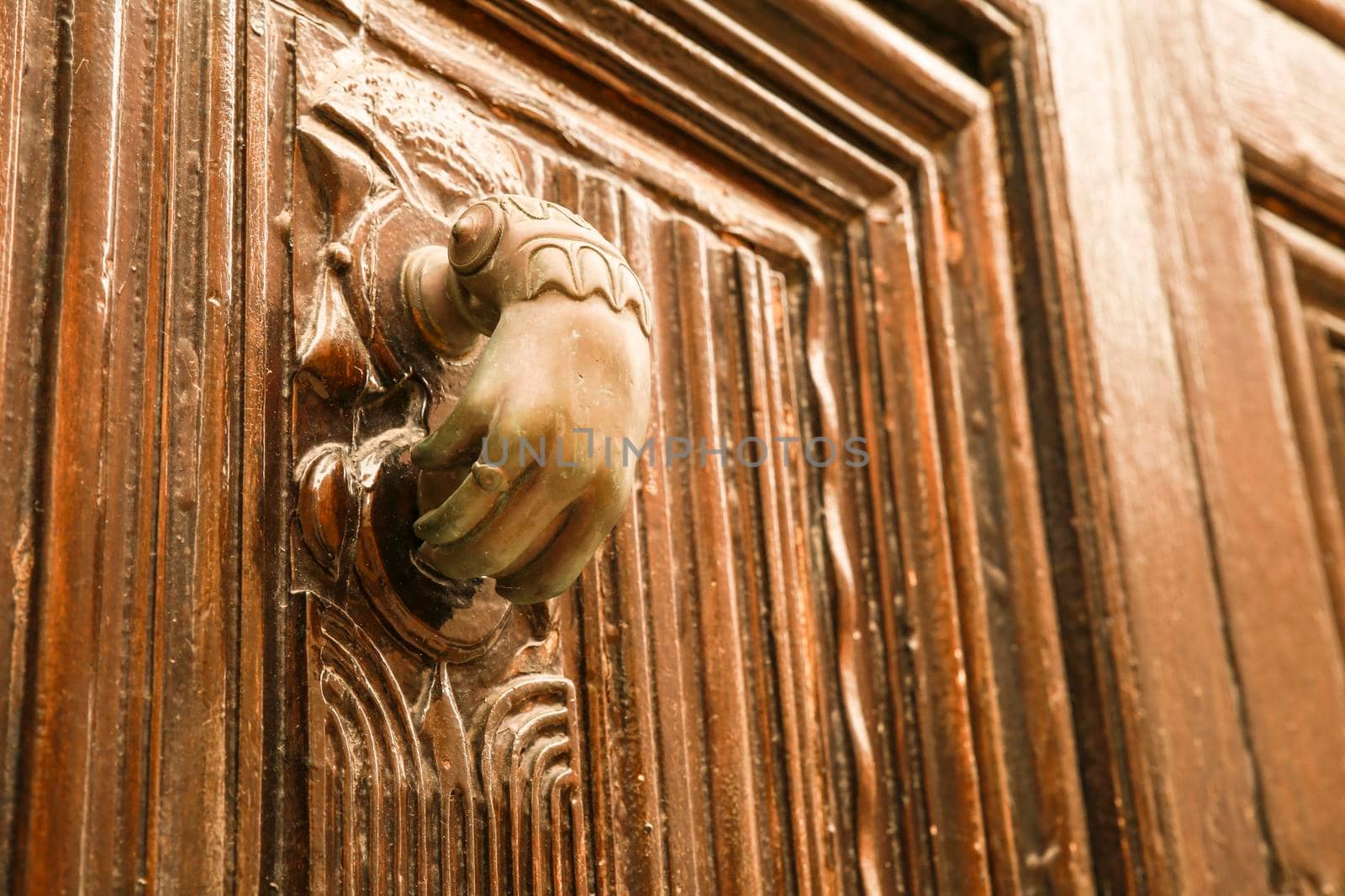 Golden doorknocker with hand shape on old wooden door by soniabonet