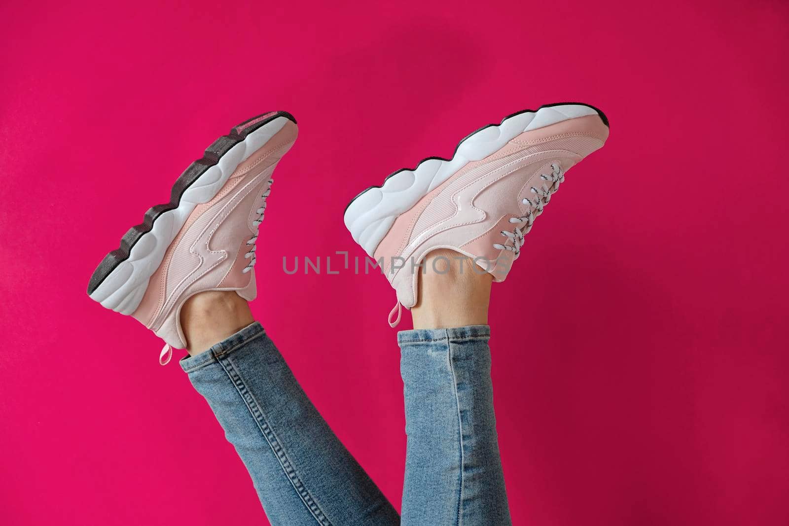 Woman's feet in unbranded modern sporty shoes on a pink background.