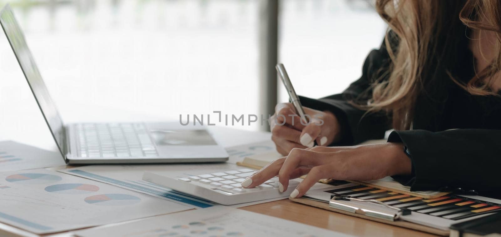 Close up of businesswoman or accountant hand holding pen working on calculator to calculate business data, accountancy document and laptop computer at office, business concept.