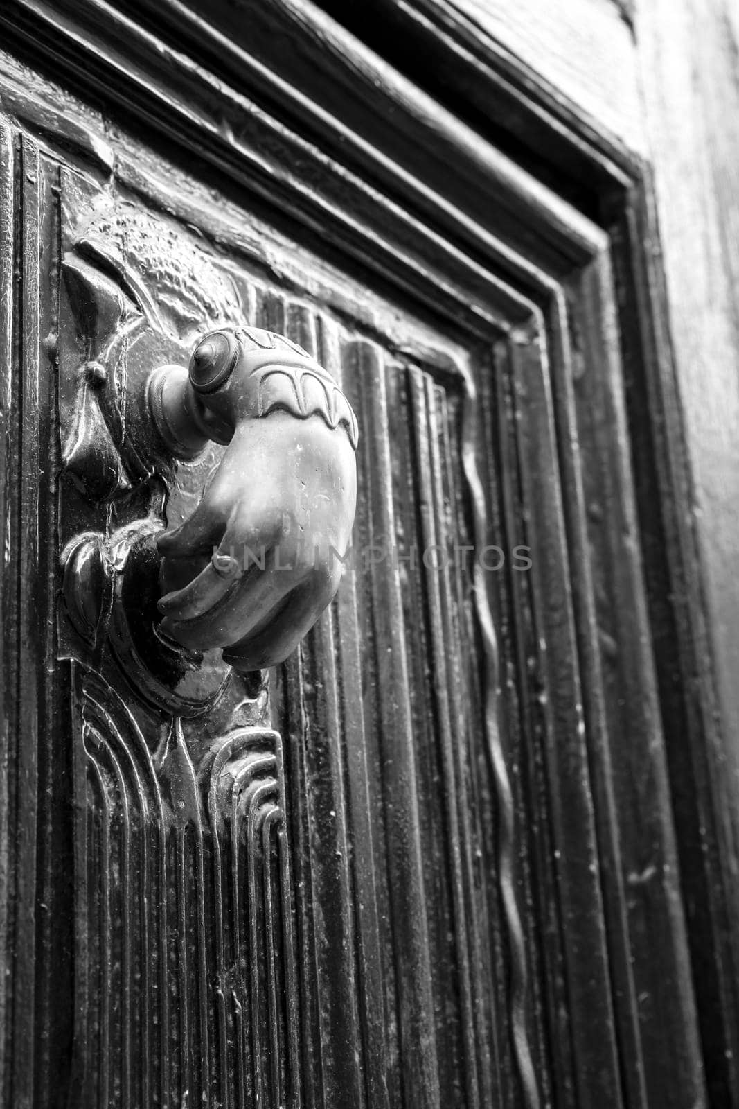 Golden doorknocker with hand shape on old wooden door by soniabonet