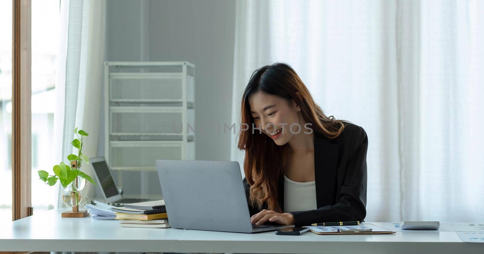 Charming asian businesswoman sitting working on laptop in office. by wichayada