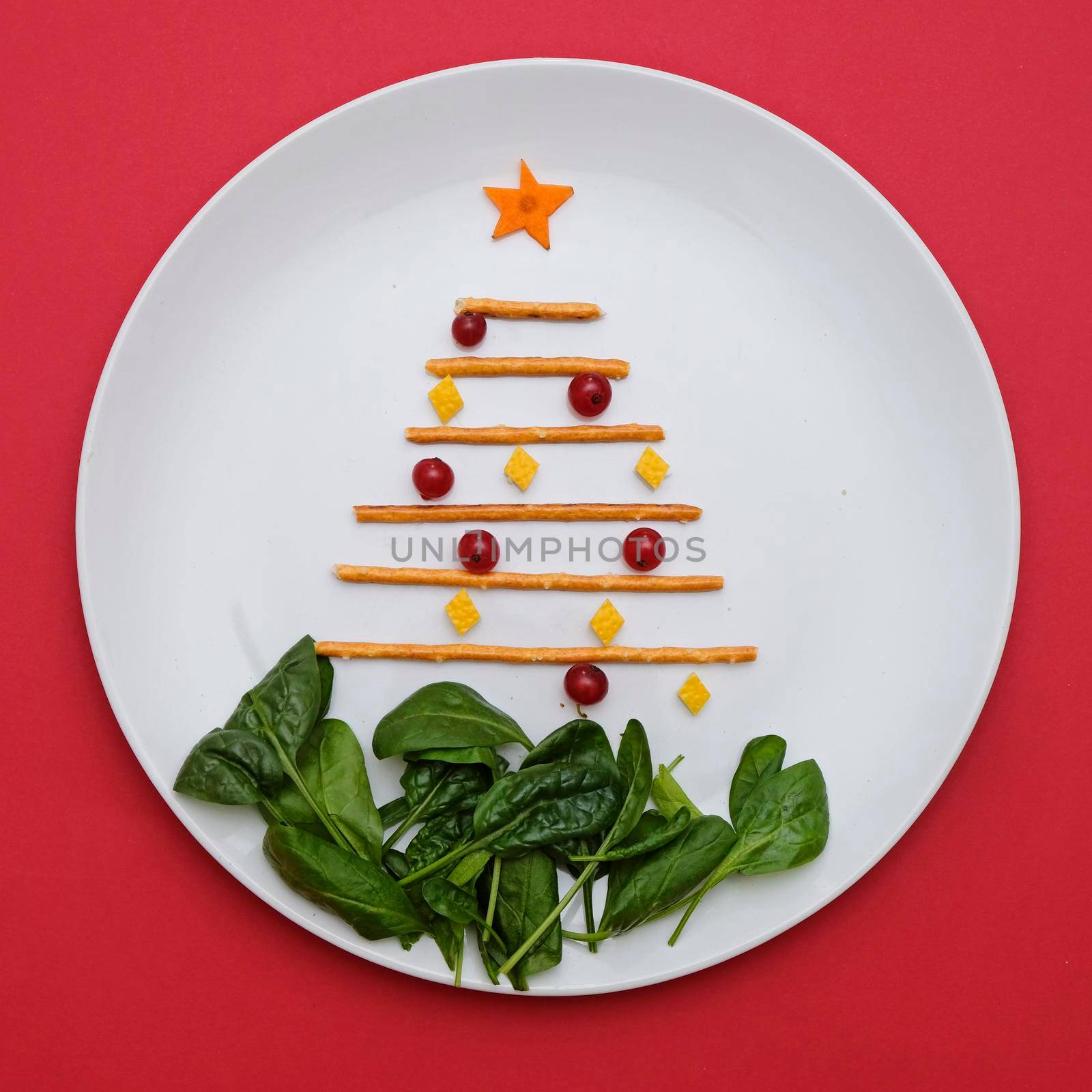 Creative edible christmas tree, food art minimalism. Food for kids and festive table. Tree made from sticks on a plate on red background. by natus111