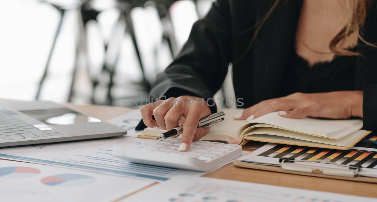 Close up of businesswoman or accountant hand holding pen working on calculator to calculate business data, accountancy document and laptop computer at office, business concept by wichayada