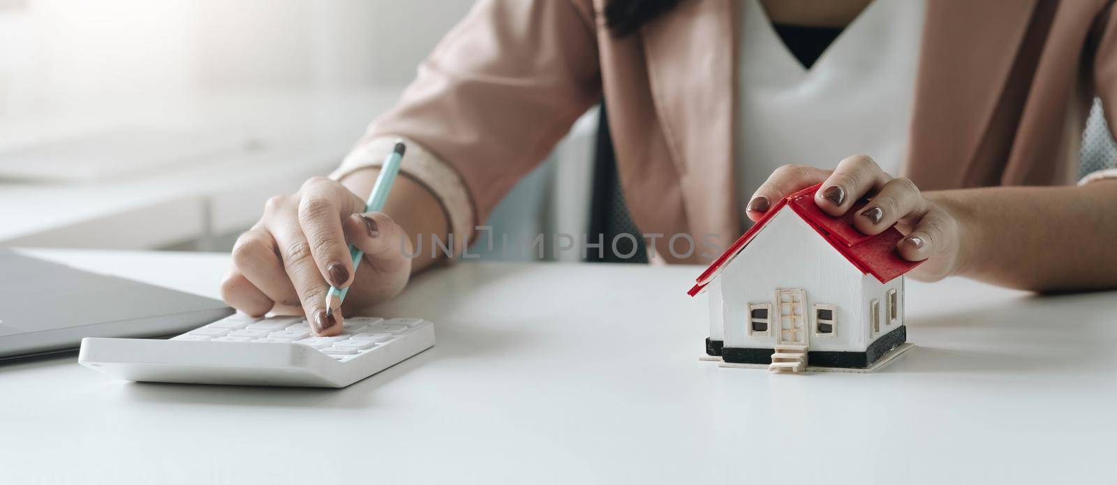 businesswoman with house model doing finances and calculate about cost to real estate investment and in other, tax system. Business Financing Accounting Banking Concept by wichayada