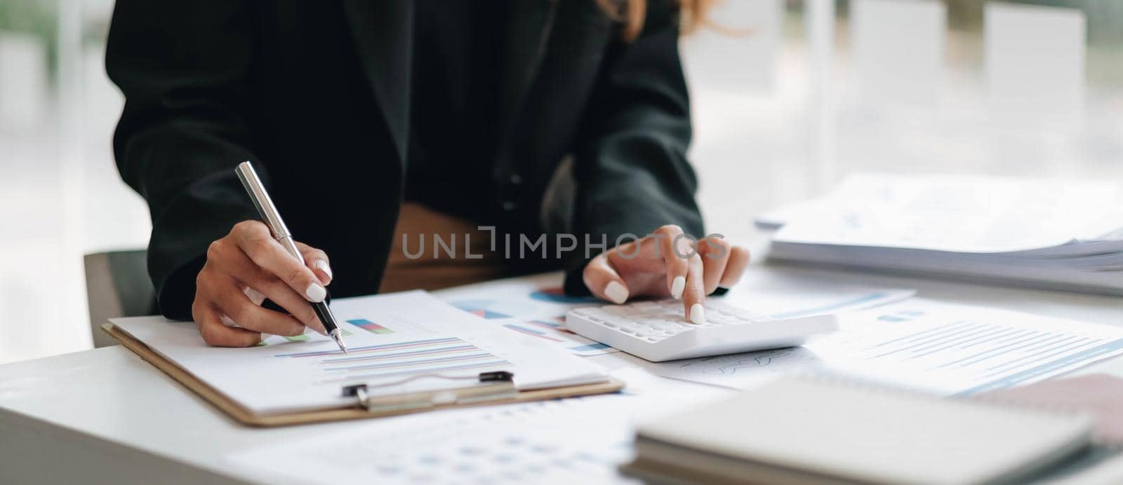 Close up of businesswoman or accountant hand holding pen working on calculator to calculate business data, accountancy document and laptop computer at office, business concept by wichayada