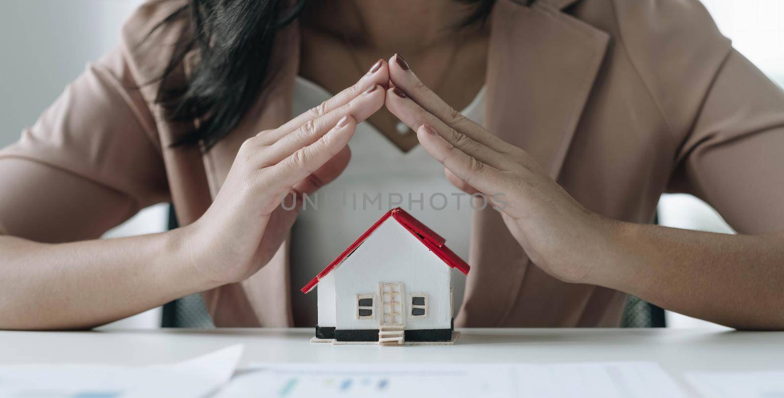 Property insurance house model protect by hand - real estate concept by wichayada