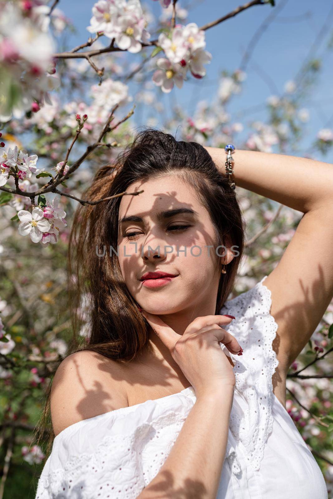 Spring concept. Nature.Young caucasian woman enjoying the flowering of an apple trees, walking in spring apple gardens. Shadow overlay on face