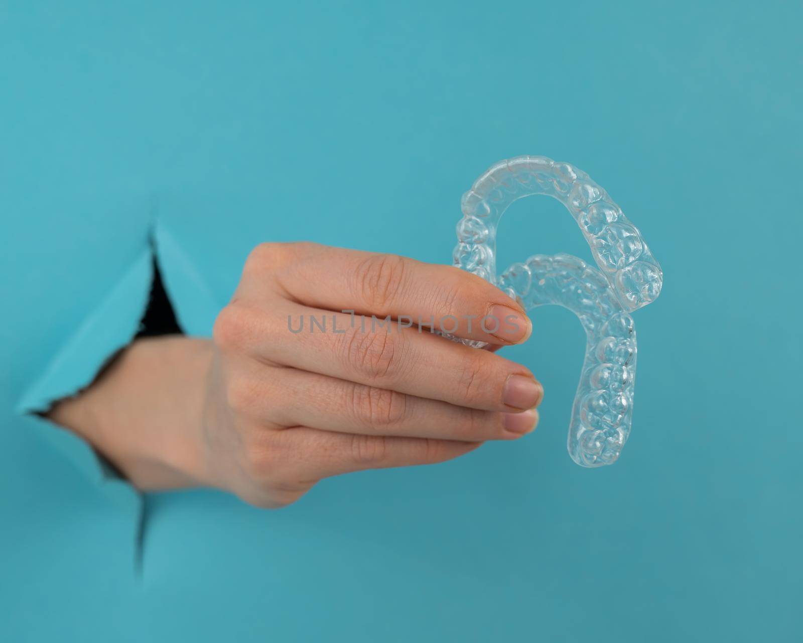 A female hand sticking out of a hole from a blue background holds removable night retainers