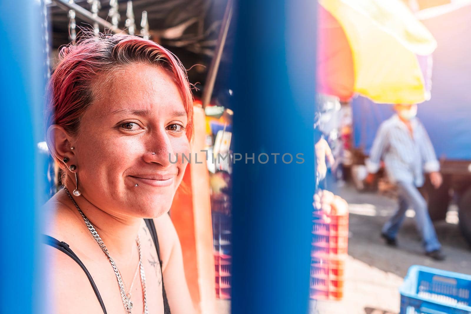 Portrait of a white Latin woman with a modern haircut with piercings on her lips and subtle tattoos looking at camera and similing in a popular market in Boaco, Nicaragua.