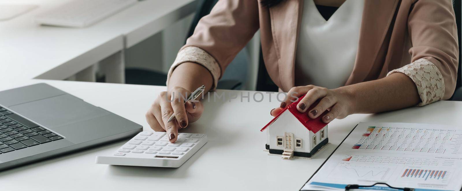 businesswoman with house model doing finances and calculate about cost to real estate investment and in other, tax system. Business Financing Accounting Banking Concept by wichayada