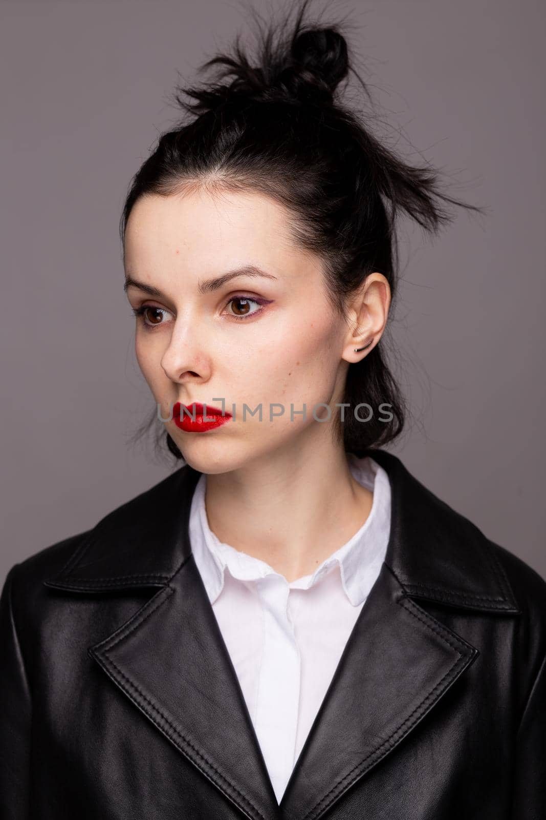 brunette woman with red lipstick on her lips in a black leather jacket and white shirt, grey background. High quality photo