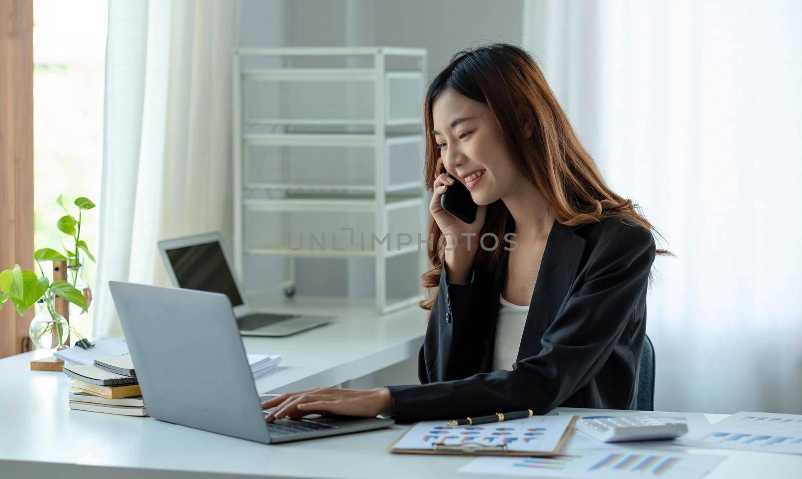 Asian business woman have the joy of talking on the phone, laptop and tablet on the office desk. by wichayada