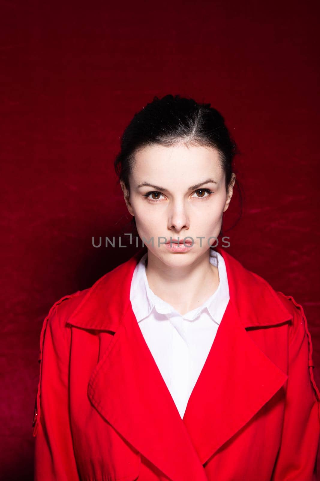 brunette woman in a white shirt red trench on a red background. High quality photo