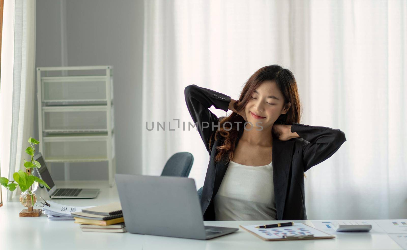 Young Asian businesswoman stretching arms raised relaxing at the office. by wichayada