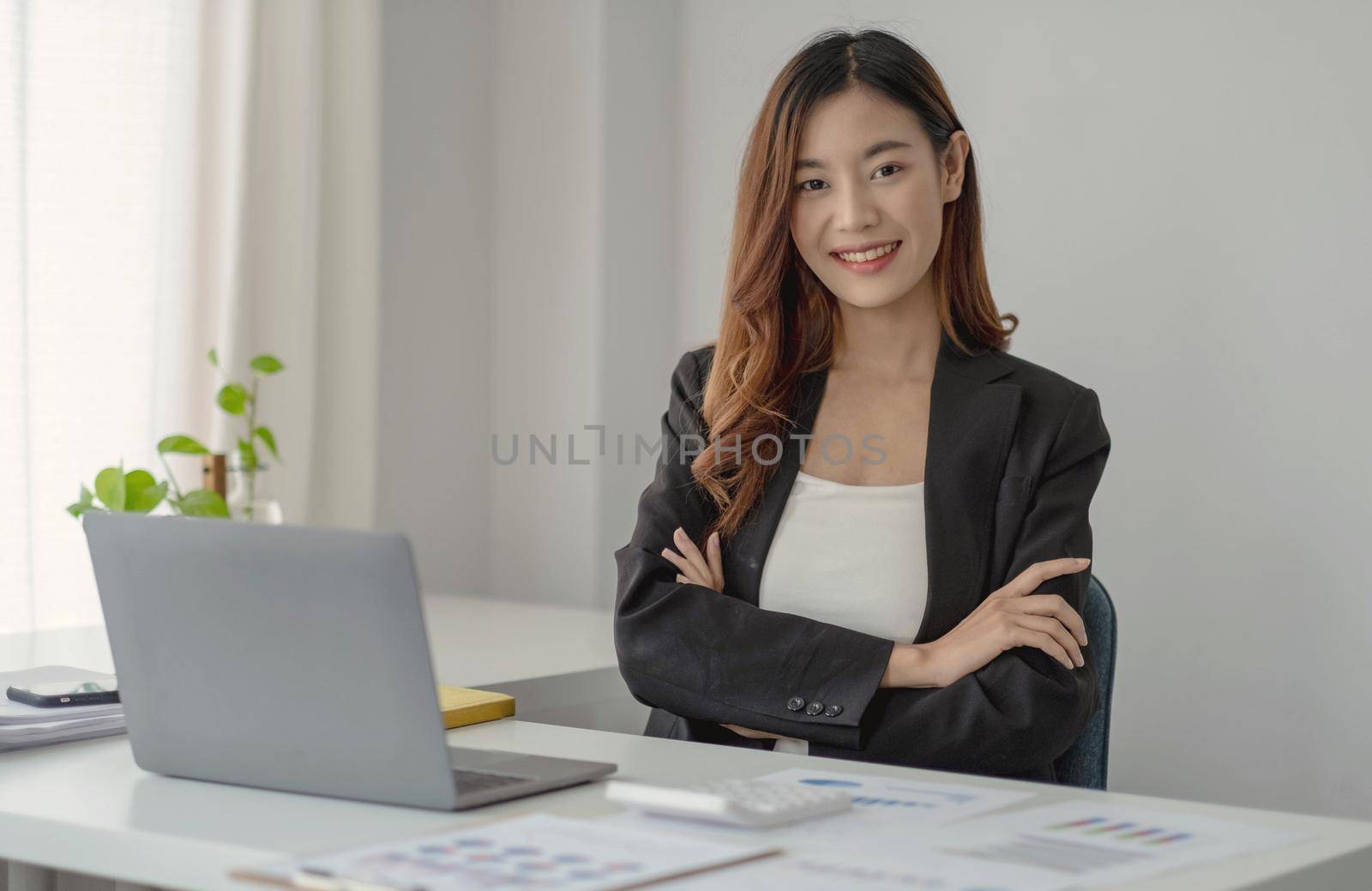 Charming Asian businesswoman working with a laptop at the office. Looking at camera. by wichayada