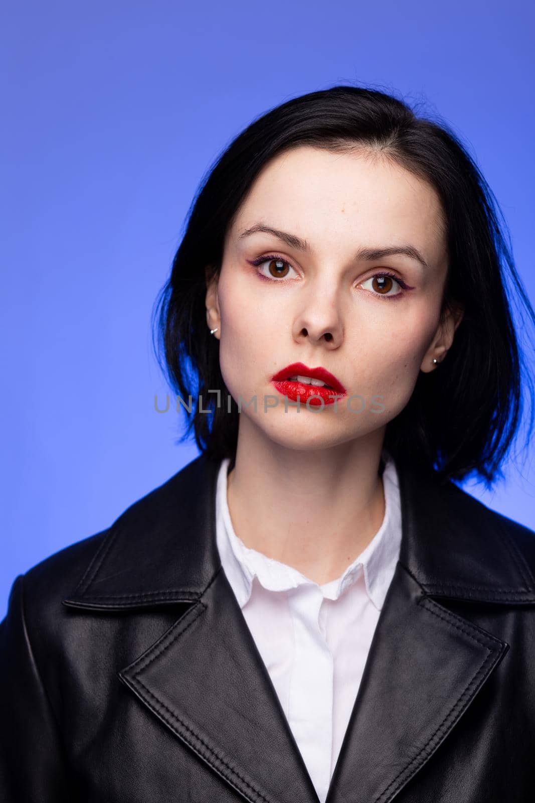 brunette woman with red lipstick on her lips in a black leather jacket and white shirt, blue background. High quality photo