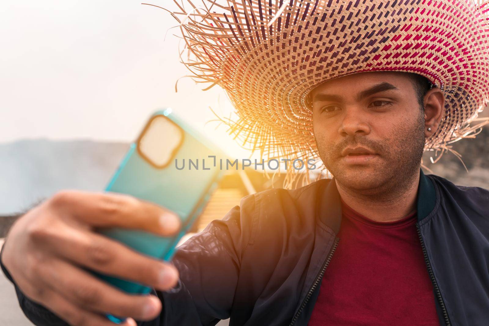 Portrait of a Latin man taking a selfie with his cell phone and wearing a colorful travel hat in an exotic tourist destination in Masaya by cfalvarez