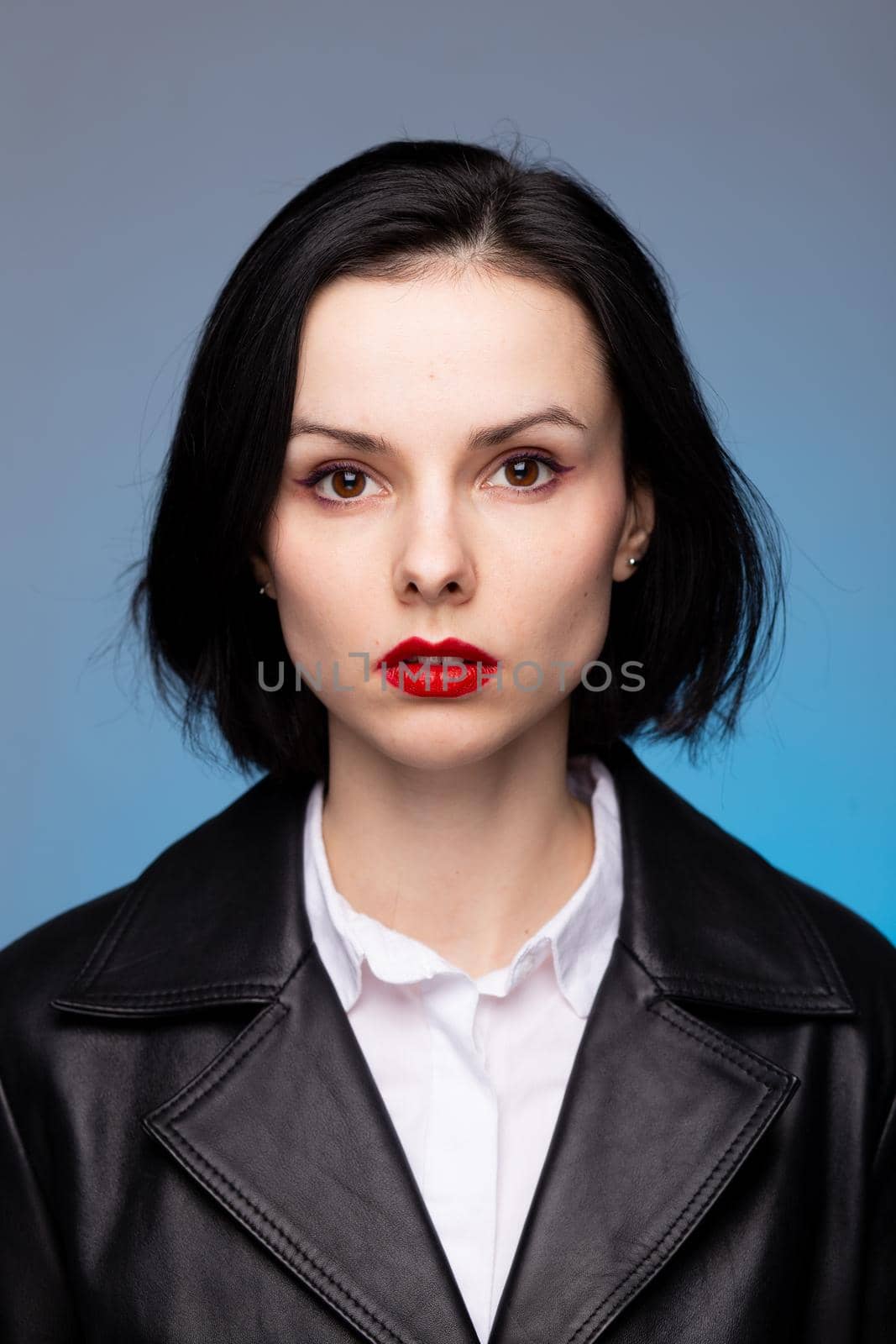 brunette woman with red lipstick on her lips in a black leather jacket and white shirt, blue background by shilovskaya