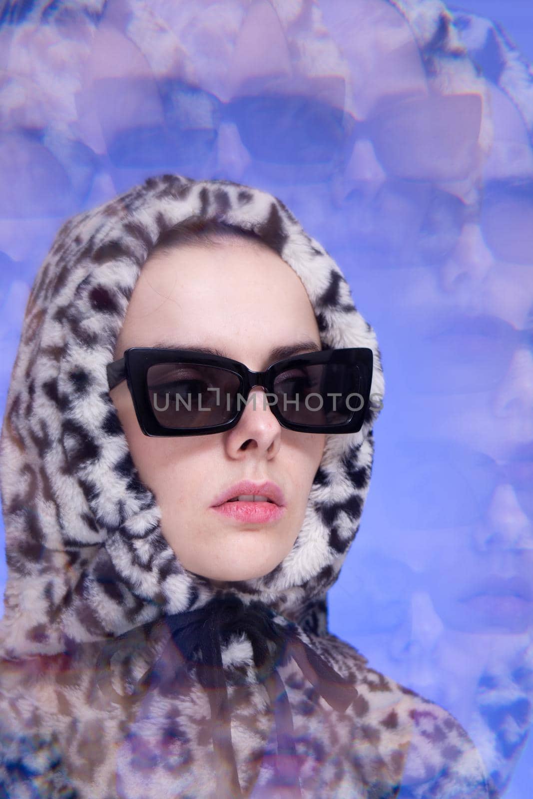 Art portrait, a woman in black glasses and a leopard hoodie on a blue background. High quality photo