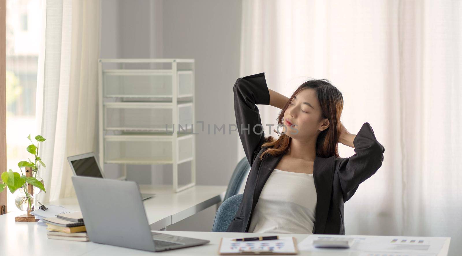 Young Asian businesswoman stretching arms raised relaxing at the office. by wichayada