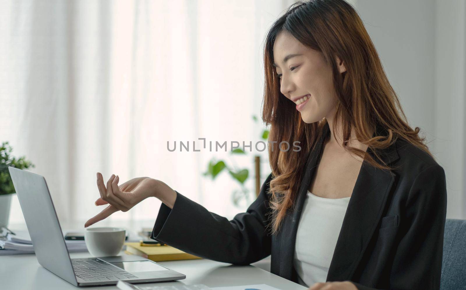 Beautiful Asian businesswoman analyzes charts using laptop calculator at the office..