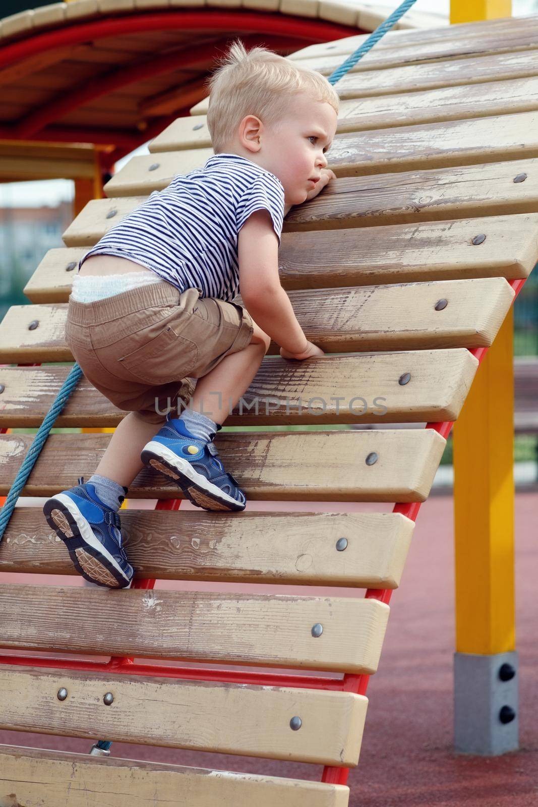 Anxious child trying not to fall down from climbing wall in a  playground. Strong and brave boy using an outdoor playground equipment