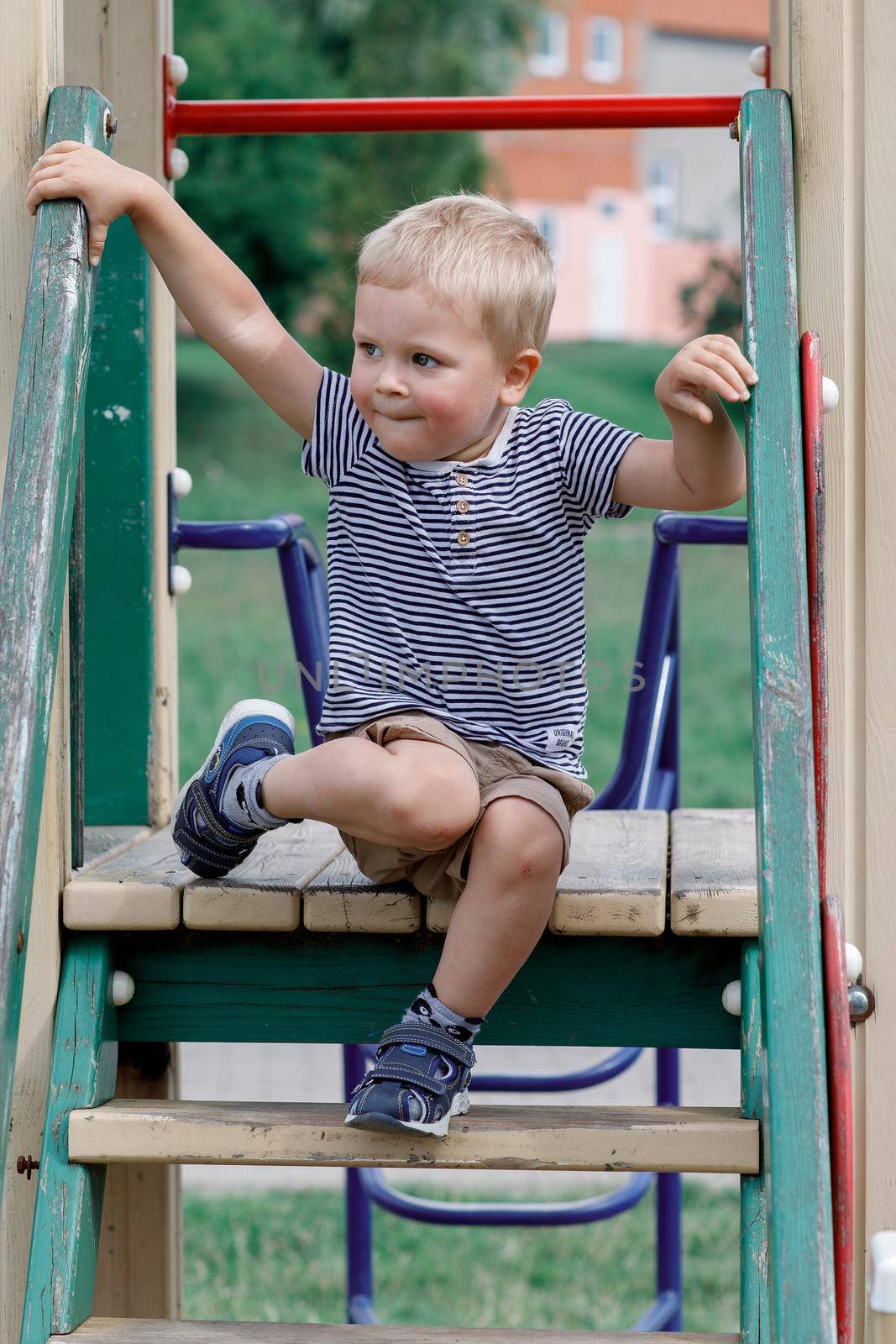 Little boy sitting on a stairs in playground. Baby boy sits down to rest before climb the stairs down. Summer activities in outdoor