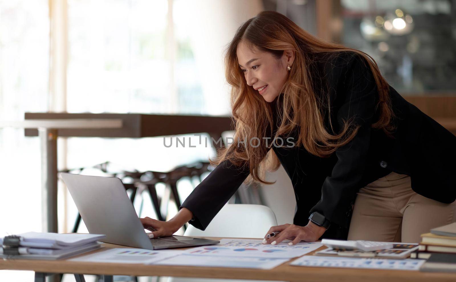 Beautiful Asian businesswoman analyzes charts using laptop calculator at the office. by wichayada