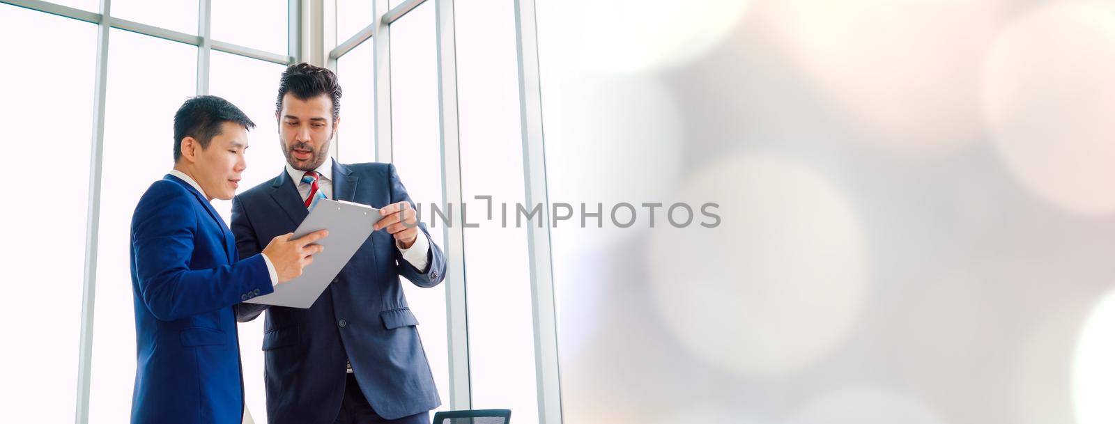 Two business people talk project strategy at office in widen view meeting room. Businessman discuss project planning with colleague at modern workplace .