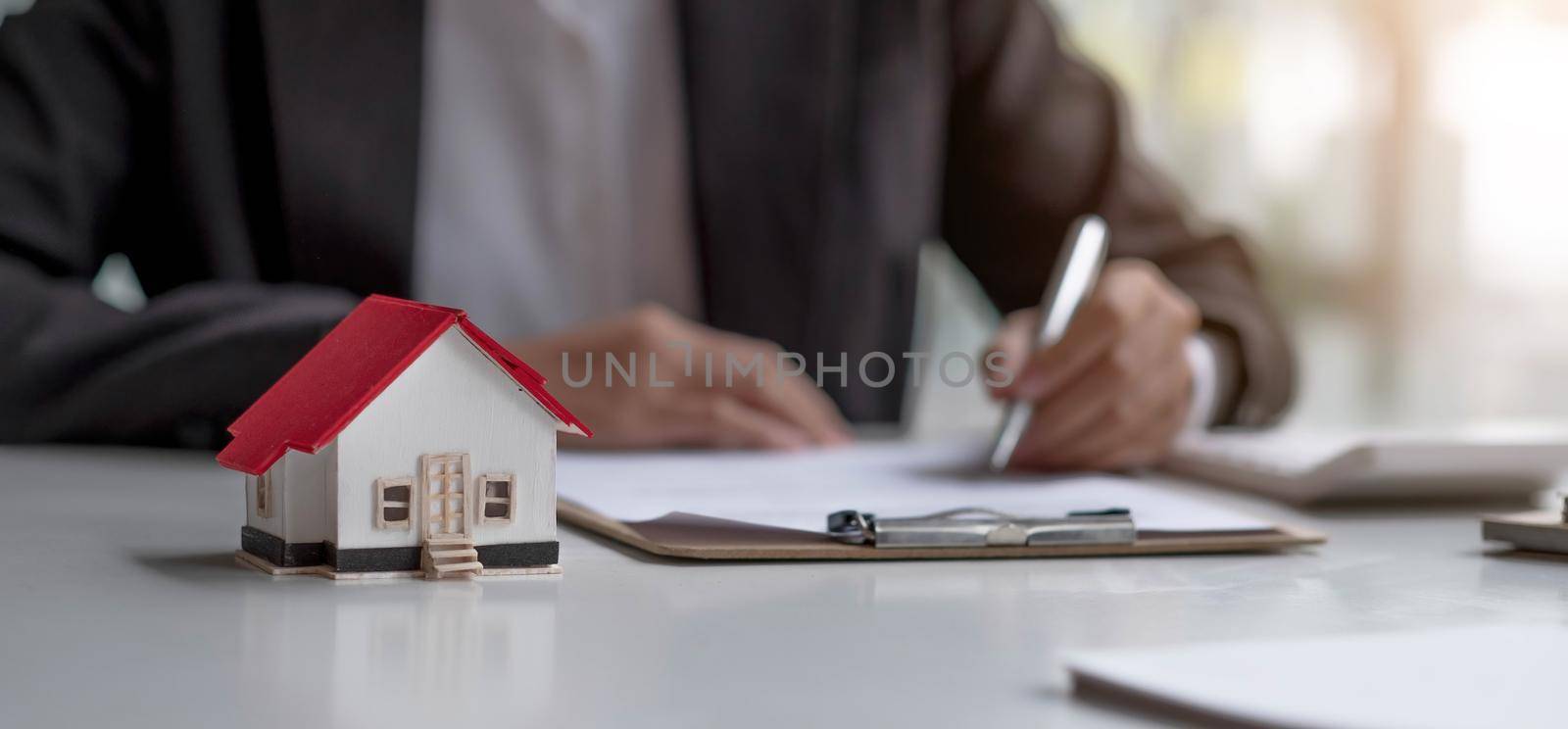 Real estate agents work at desks in rooms with paperwork and house designs to introduce clients..