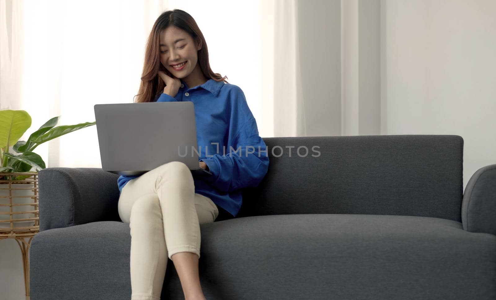 Young business freelance Asian woman working on laptop checking social media while lying on the sofa when relax in living room at home. by wichayada