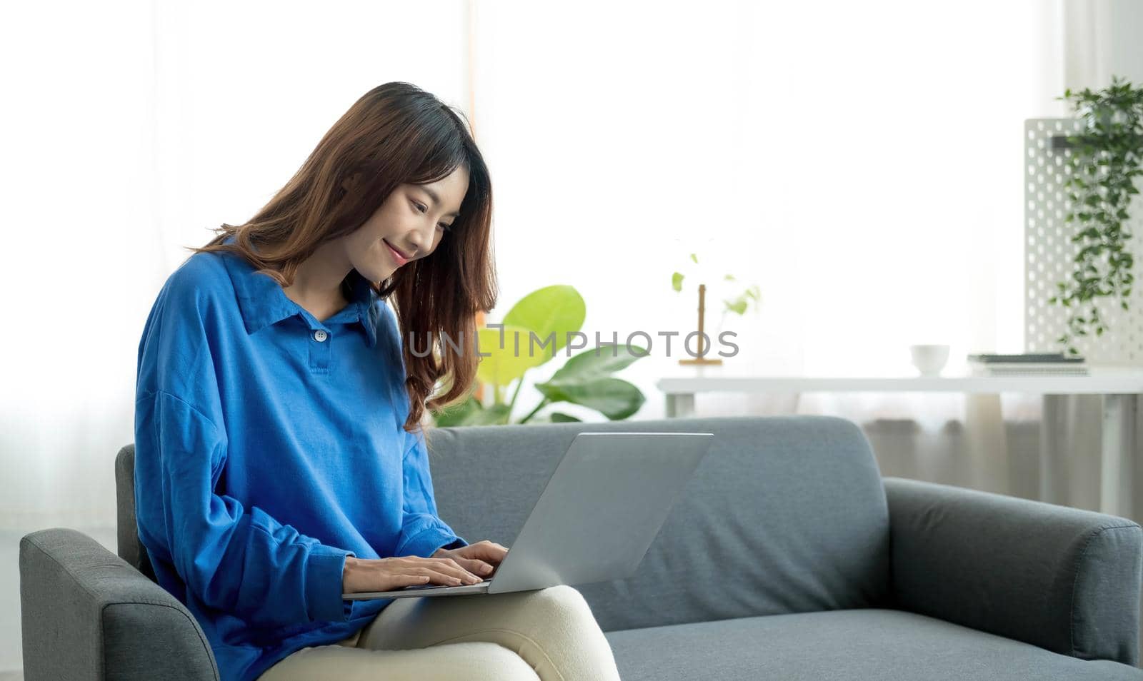 Young business freelance Asian woman working on laptop checking social media while lying on the sofa when relax in living room at home. by wichayada