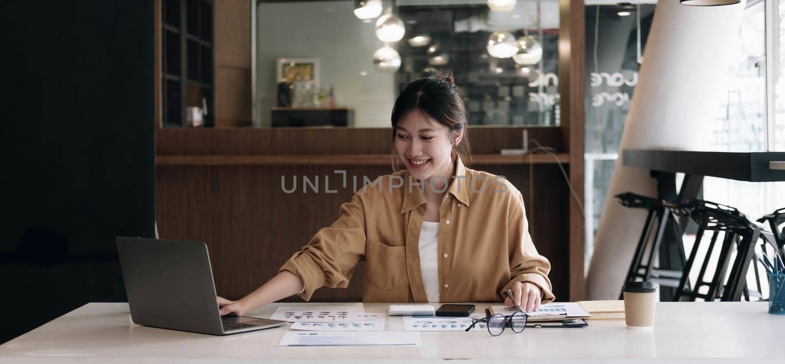 Happy young asian businesswoman sitting on her workplace in the office. Young woman working at laptop in the office..