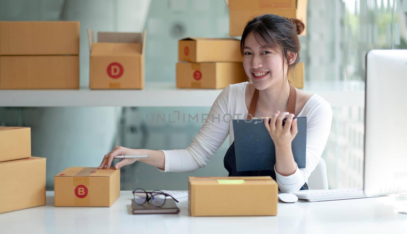 Portrait young asia female owner startup look at camera work happy with box at home prepare parcel delivery in sme supply chain, procurement, omnichannel ecommerce online concept. by wichayada