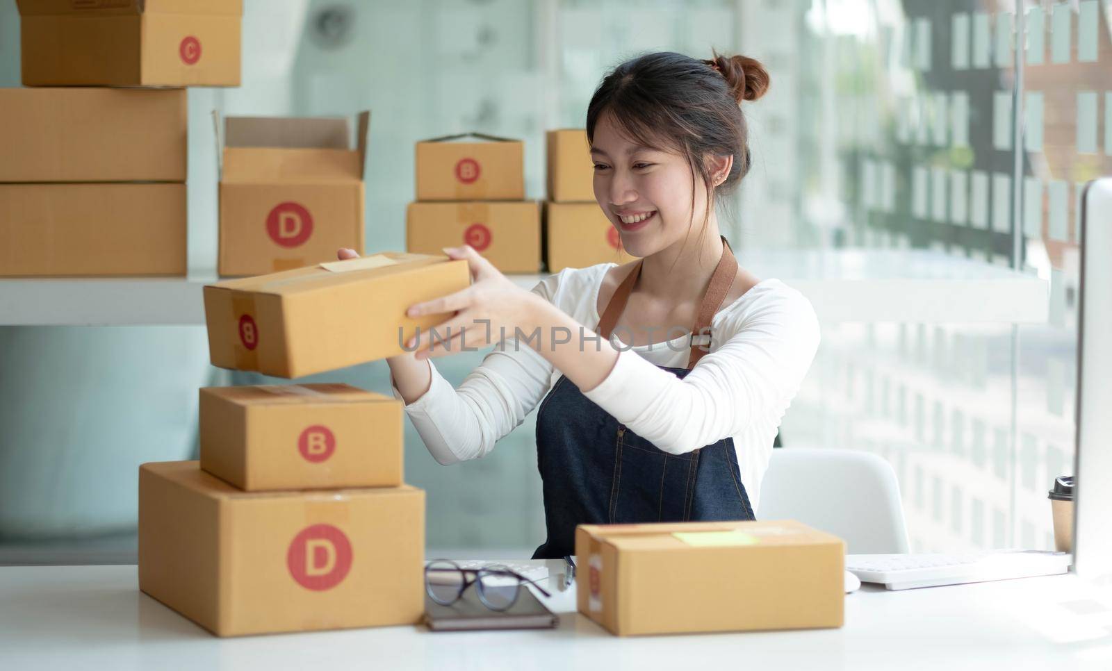 Smiling young Asian business owner woman prepare parcel box and standing check online orders of product for deliver to customer on laptop computer. Shopping Online concept..