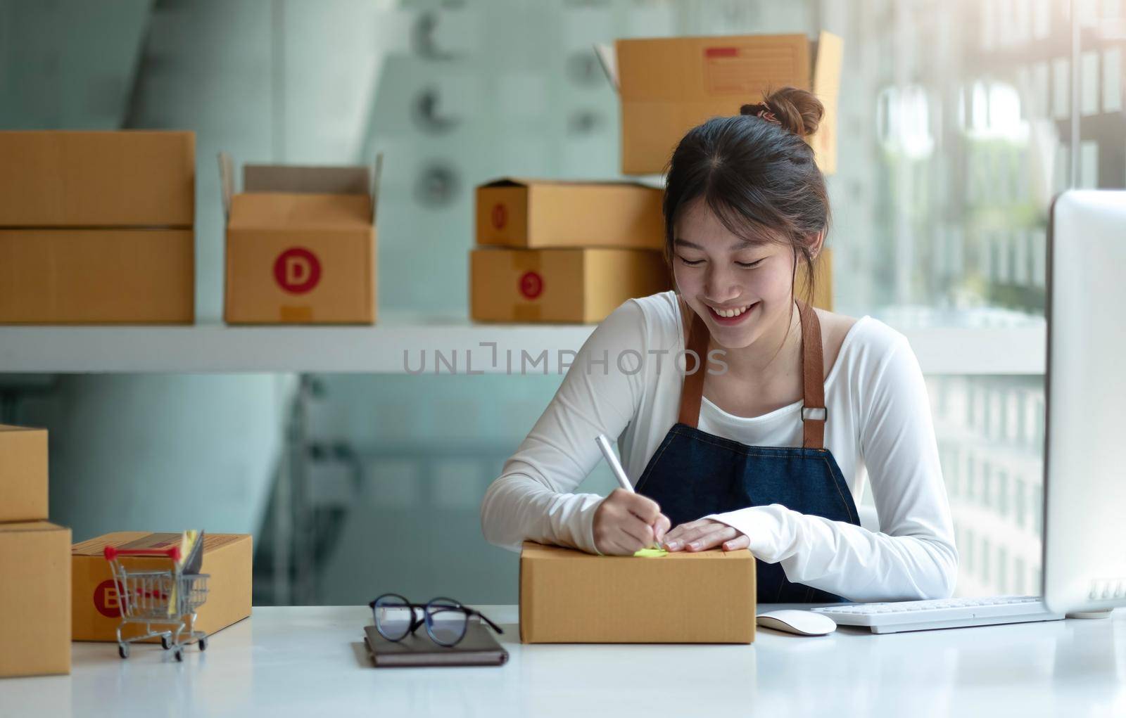 Asian Small business entrepreneur SME writing address on cardboard box at workplace small business entrepreneur SME , working with box at home. by wichayada