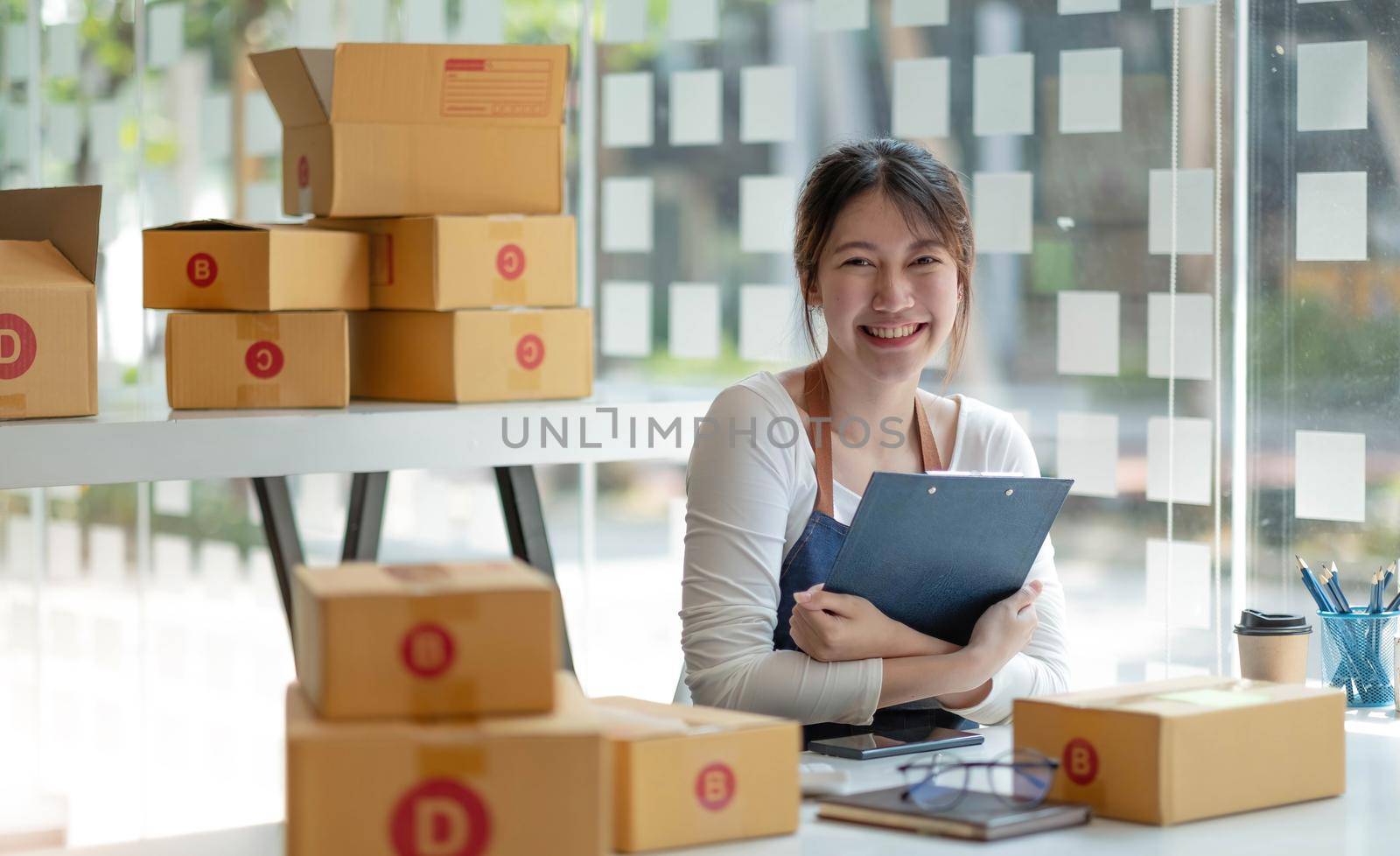 Young business woman working online e-commerce shopping at her shop. Young woman seller prepare parcel box of product for deliver to customer. Online selling, e-commerce..