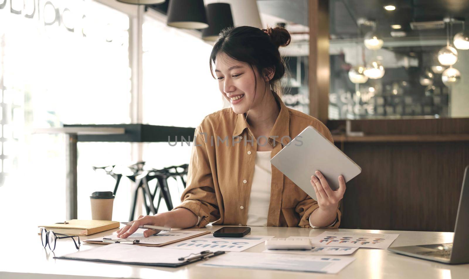 Charming Asian woman with a smile standing holding tablet and point graph at the office. by wichayada