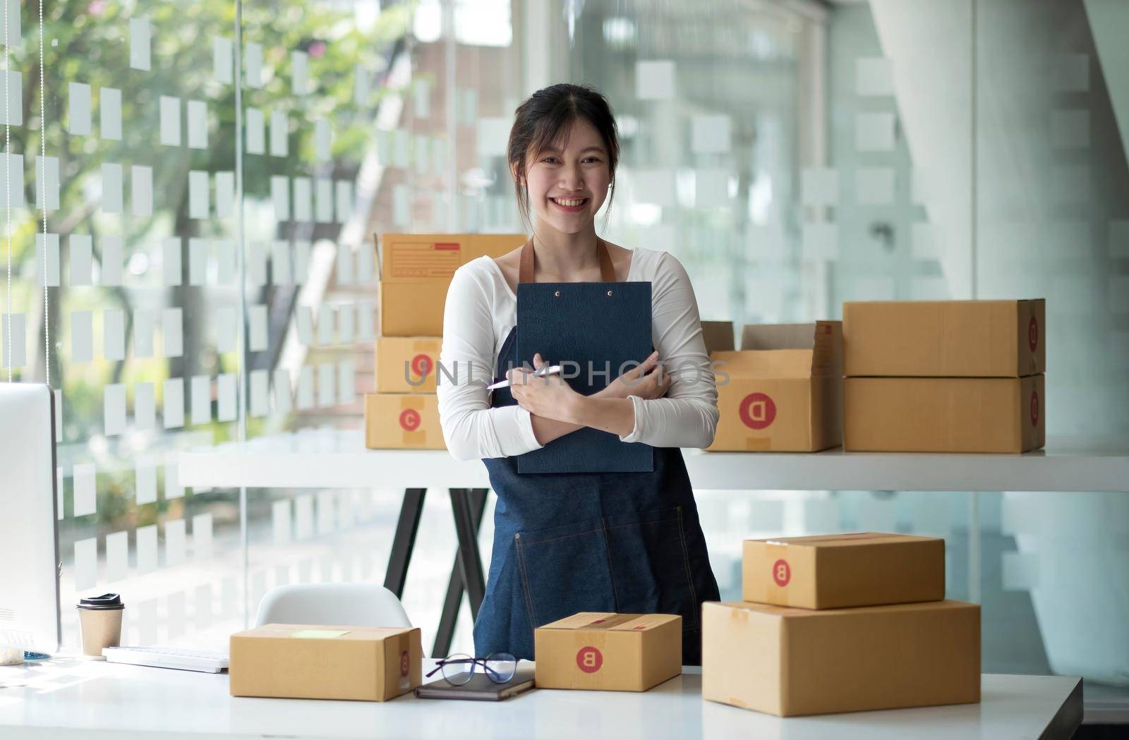 Young business woman working online e-commerce shopping at her shop. Young woman seller prepare parcel box of product for deliver to customer. Online selling, e-commerce. by wichayada