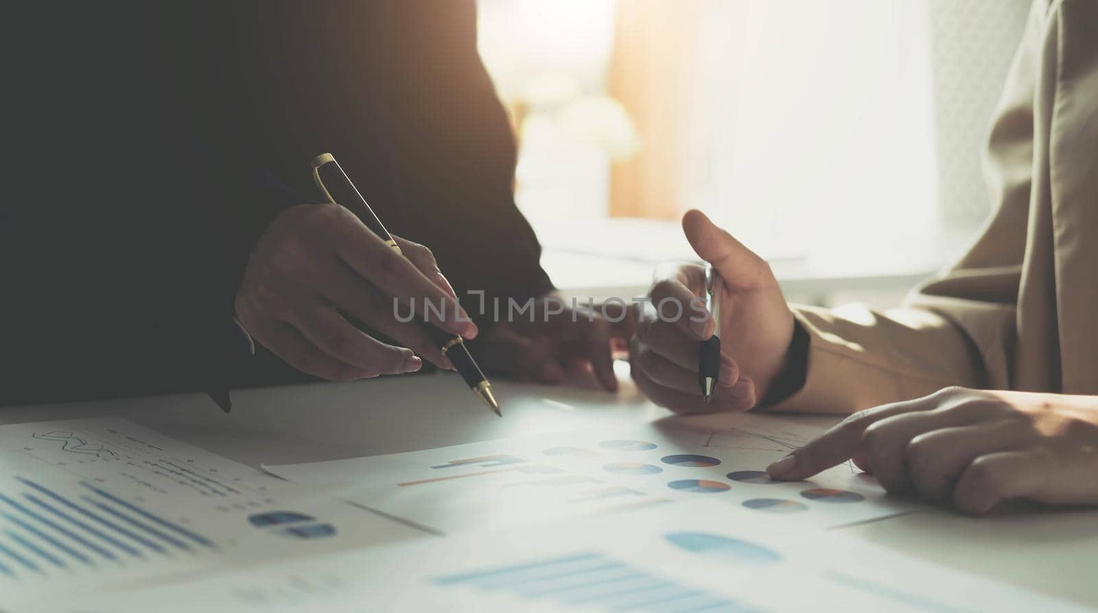 Hands of two young financiers sitting by workplace and discussing financial papers and data at working meeting by wichayada