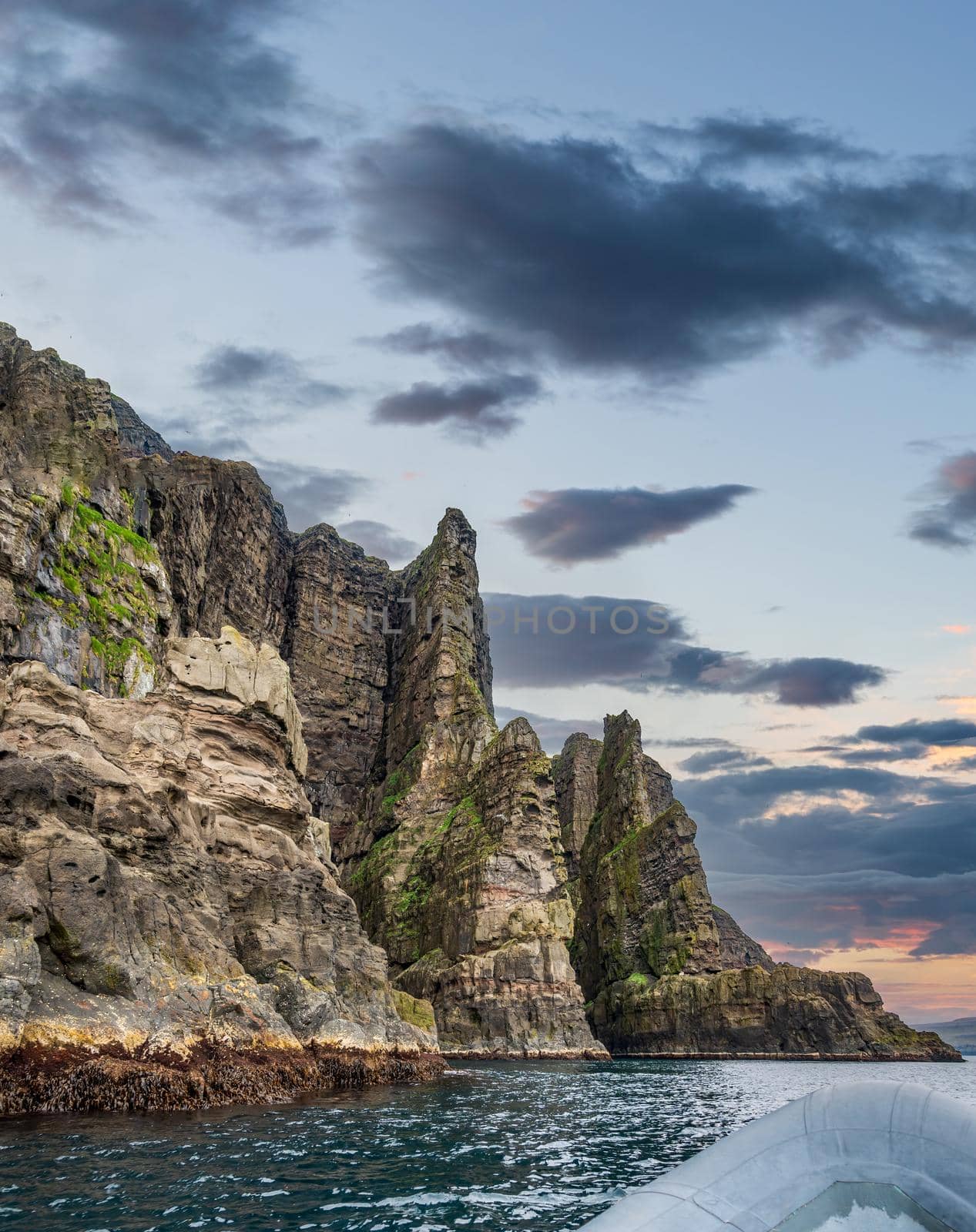 Motorboat sailing towards huge cliffs under cloudy sky for text space