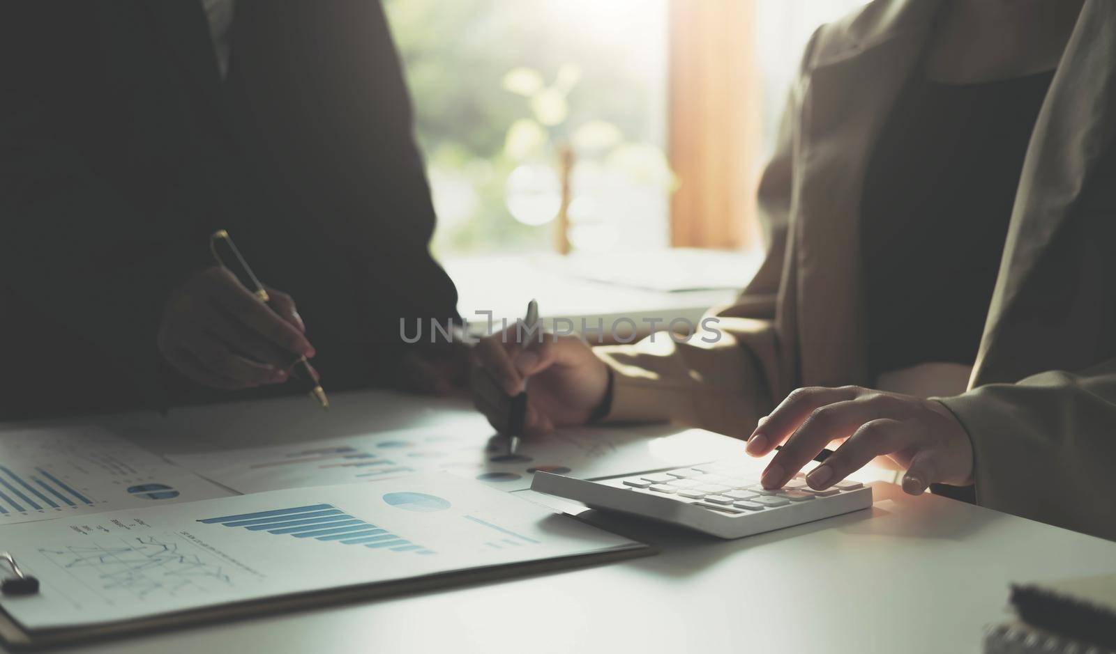 Close-up Hands of two young woman accountant use calculator with holding pen and point report in the office . finance and accounting concept by wichayada