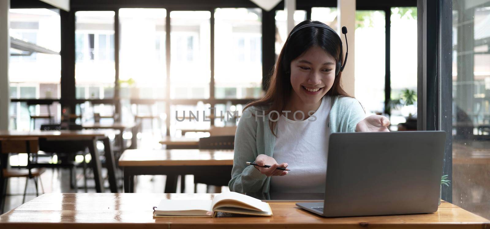 Happy young woman in headphones speaking looking at laptop making notes, girl student talking by video conference call, female teacher trainer tutoring by webcam, online training, e-coaching concept by wichayada