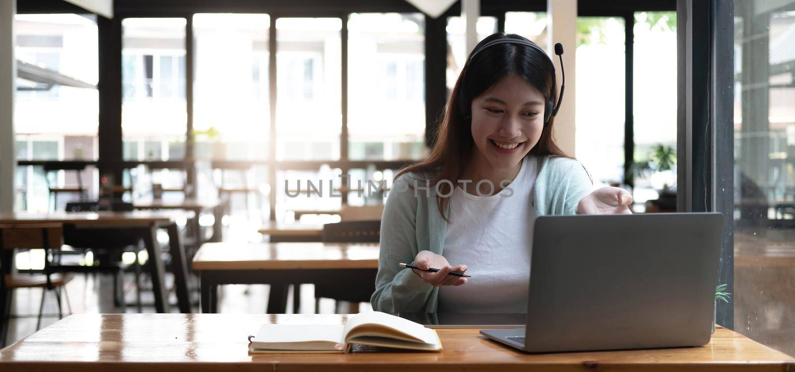 Happy young woman in headphones speaking looking at laptop making notes, girl student talking by video conference call, female teacher trainer tutoring by webcam, online training, e-coaching concept.