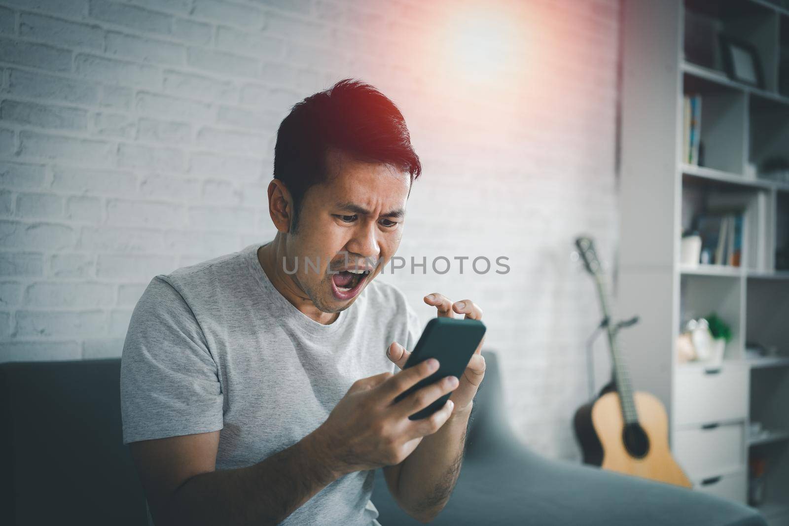 Depression concept. Asian man sad and checking mobile phone sitting on the sofa in the living room at home, Asian man serious and worry while using mobile phone. by Wmpix