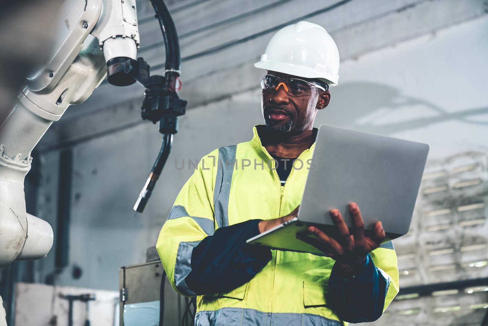African American factory worker working with adept robotic arm in a workshop . Industry robot programming software for automated manufacturing technology .