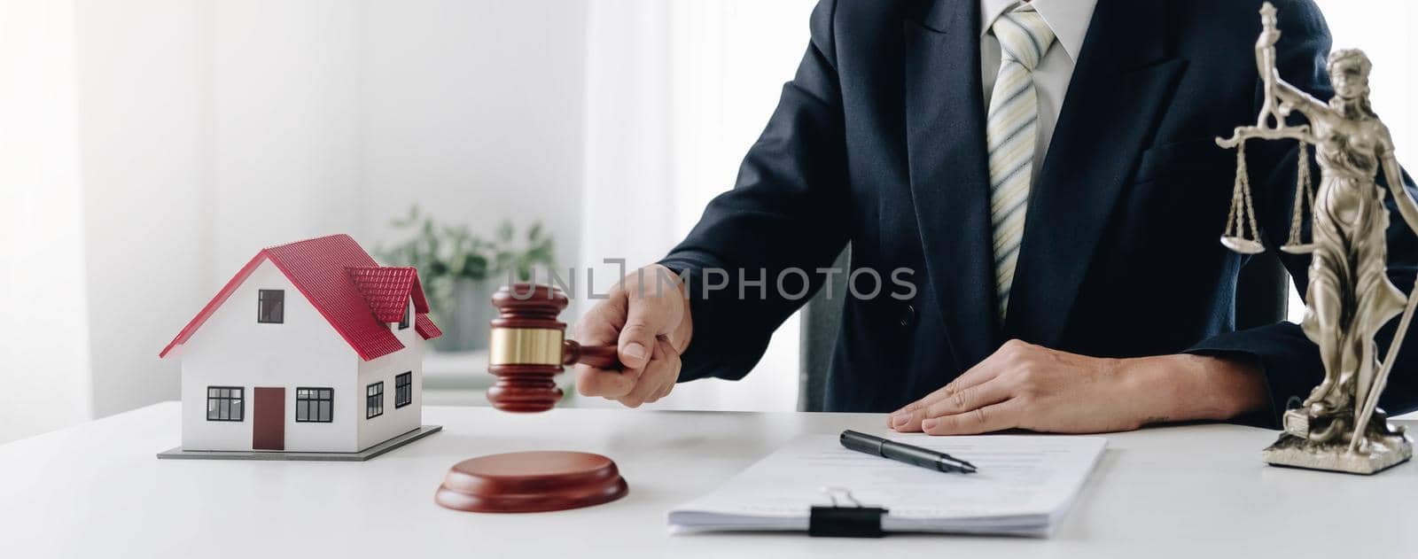 Stern judge with paper document pronouncing sentence in a court of law. Judge finds the accused guilty, passes judgement and rules case closed. Hand holding gavel and hitting sound block in close-up by wichayada