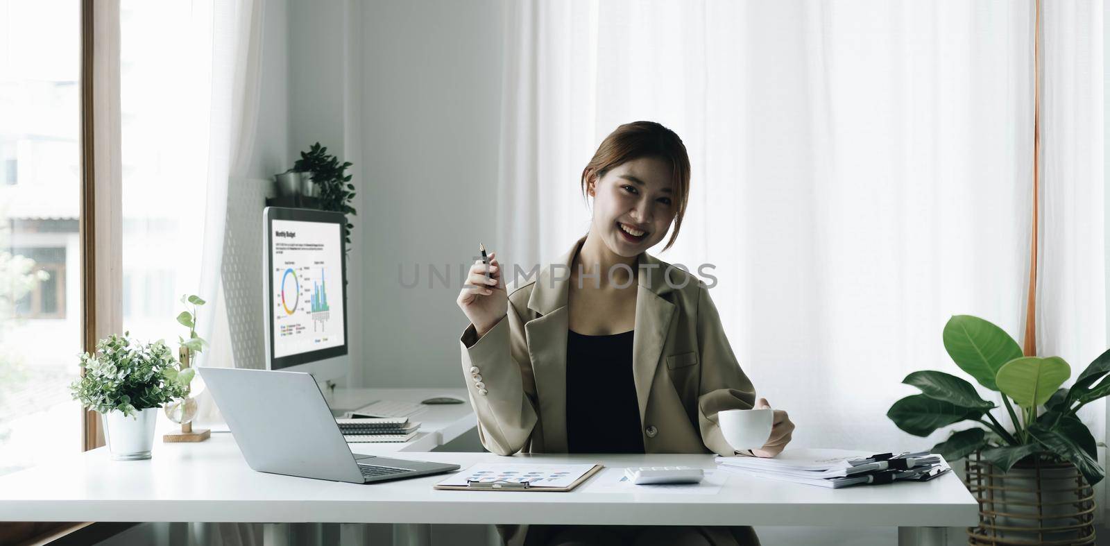 Smiling Asian businesswoman holding a coffee mug and laptop at the office. Looking at the camera. by wichayada
