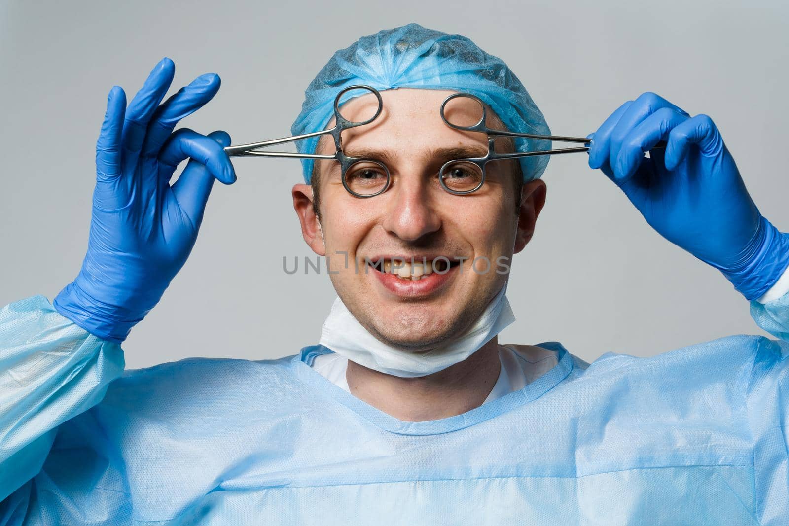 Wacky smiling doctor surgeon with crazy emotions. Young doctor holding medical scissors. by Rabizo
